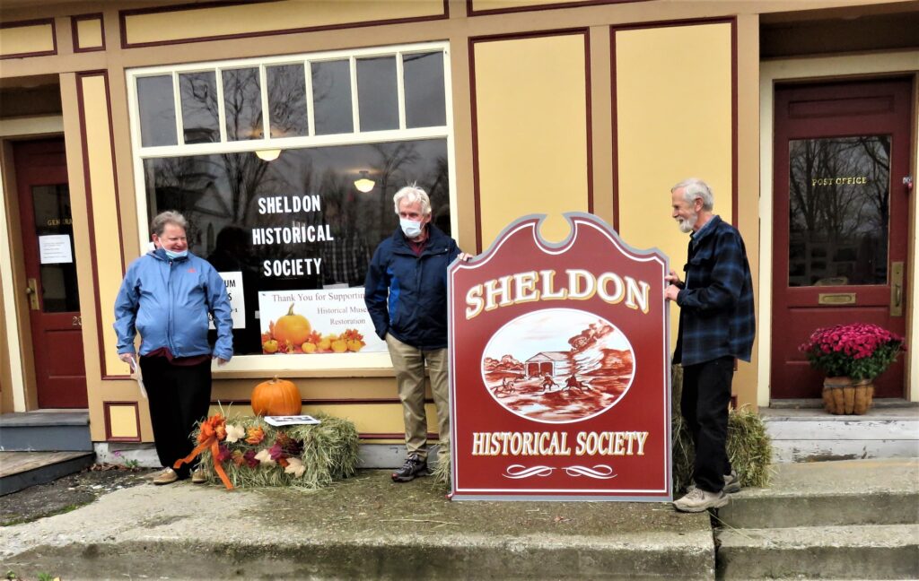 The new Sheldon museum sign with 3 people standing by it